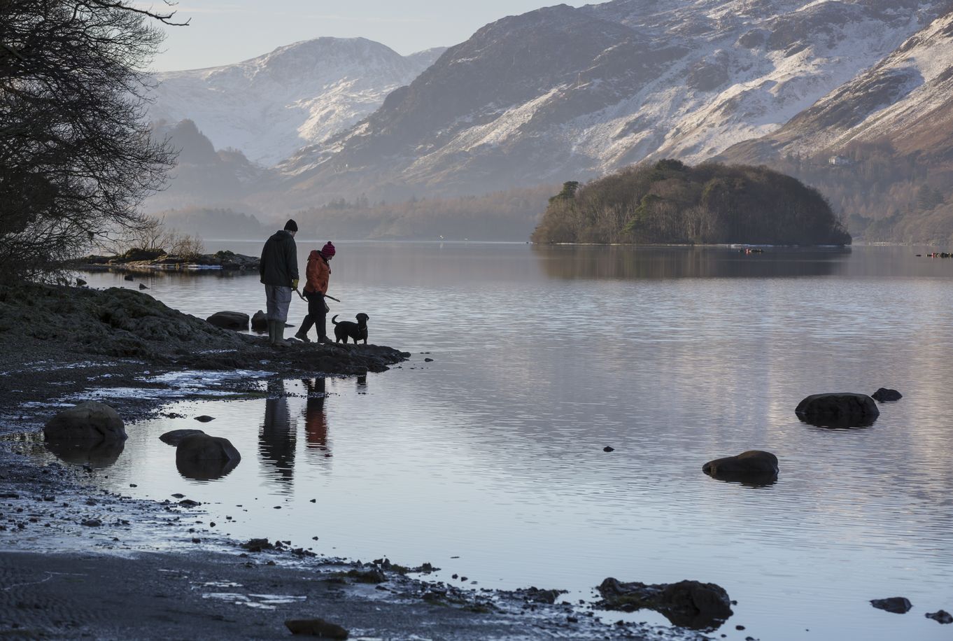 Couple with dog walking on the shores of Derwentwater in winter