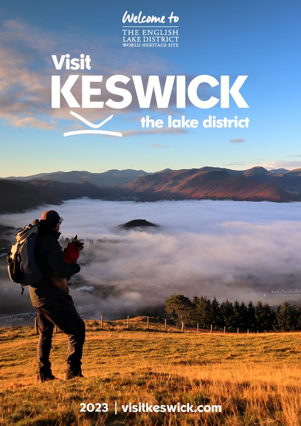 Visit Keswick Guide cover.  Man holding small dog looking towards Keswick and Derwentwater, both hidden beneath a cloud inversion.
